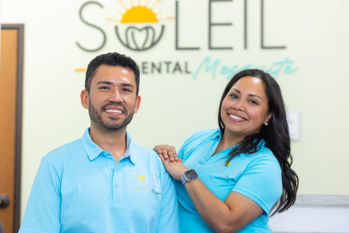 La Dra. Diana Vazquez y el Dr. Jose Aldana frente al muro con el logo de Soleil Dental Mesquite