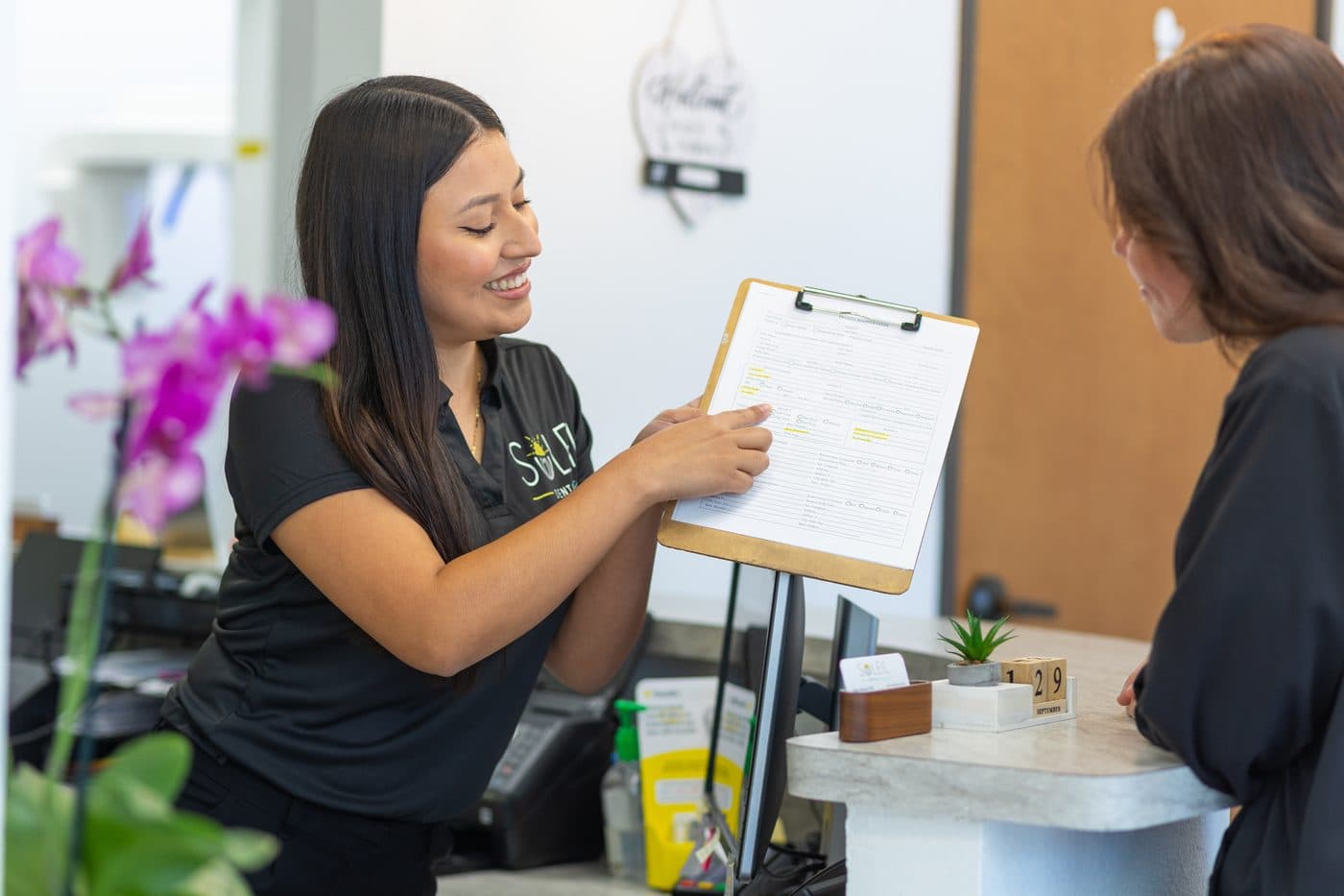 A Soleil Dental Mesquite front desk team member going over a form on a clipboard with a patient