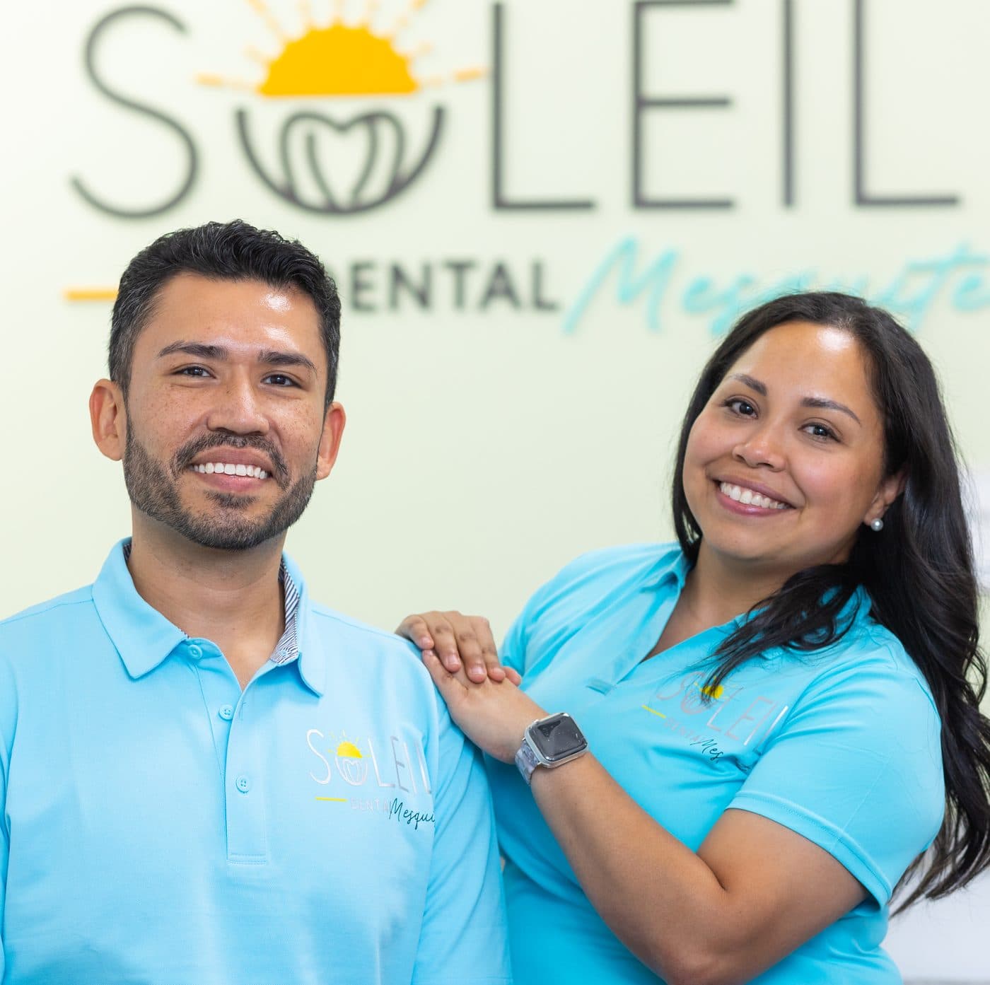 La Dra. Diana Vazquez y el Dr. Jose Aldana, los dentistas dueños de Soleil Dental Mesquite, frente al muro con el logo de la oficina