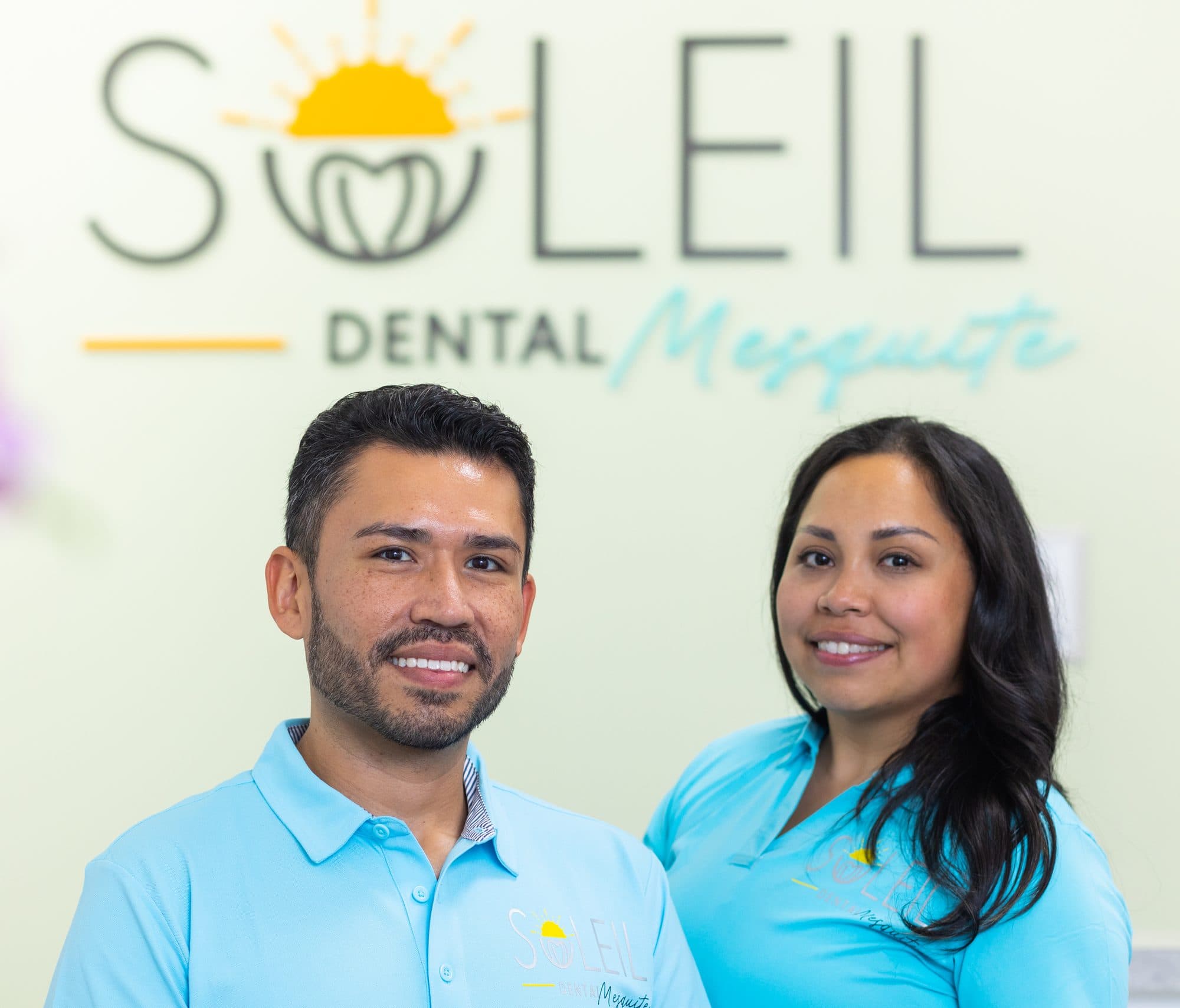 Dr. Diana Vazquez and Dr. Jose Aldana, the dentists who own Soleil Dental Mesquite, in front of the office logo wall