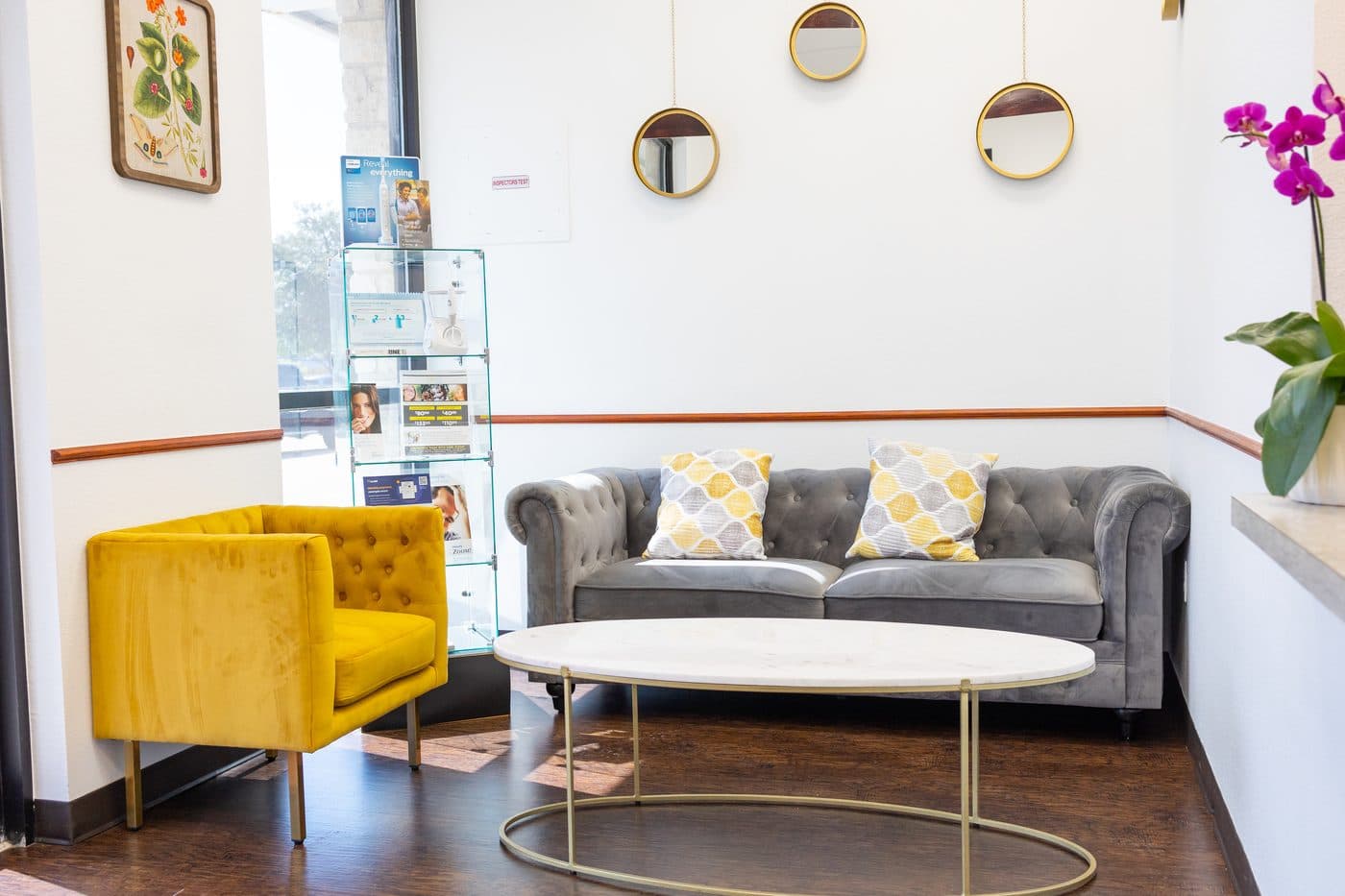 The waiting room: a yellow velvet chair, a gray sofa and round mirrors on the wall