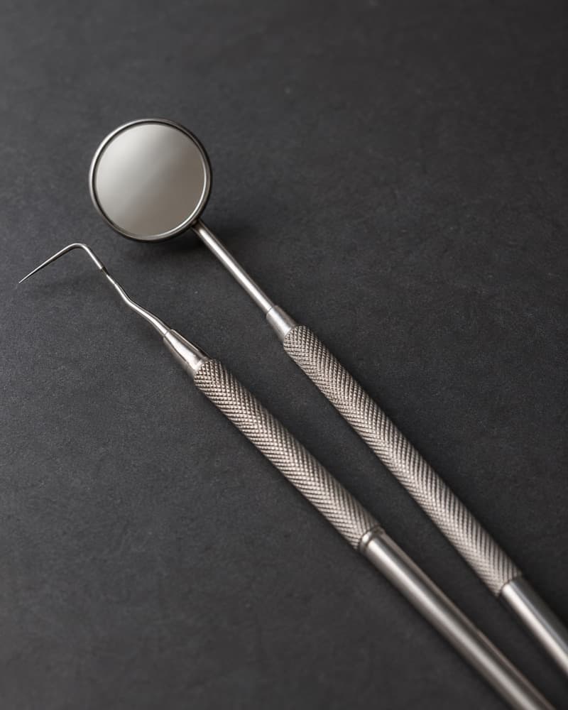 Un espejo dental y un explorador sobre una superficie oscura