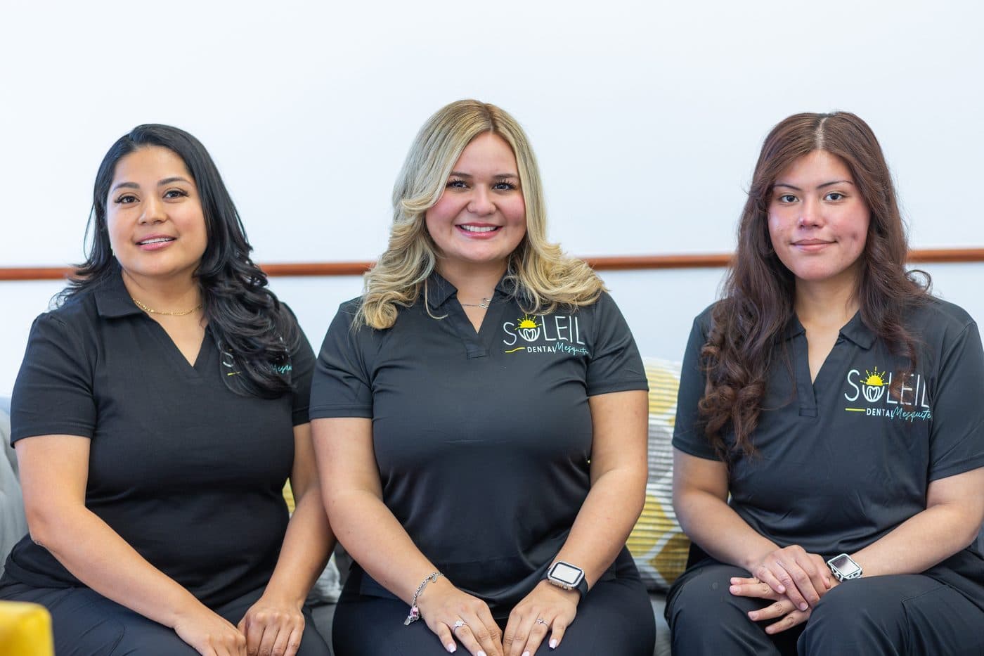 Tres integrantes del equipo de Soleil Dental Mesquite sonriendo en el sofá de la sala de espera