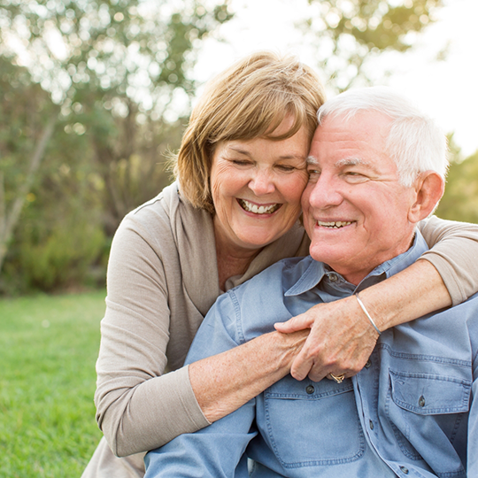 Senior man and woman hugging outdoors and smiling with dentures in Mesquite