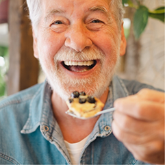 Smiling senior man holding a fork full of food near his mouth