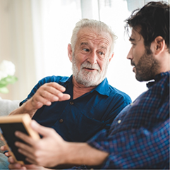 Senior man talking to the younger man sitting next to him on a couch