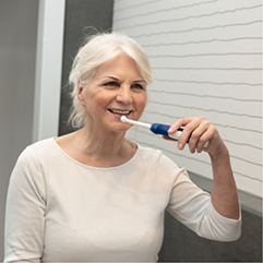 Senior woman smiling while brushing her teeth