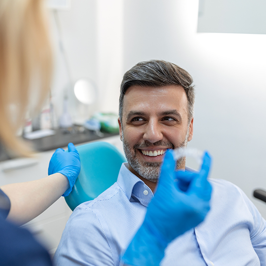 Dentist showing an Invisalign clear aligner to a man in the dental chair