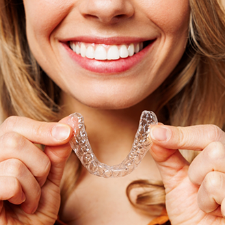 Smiling woman holding an Invisalign aligner near her mouth