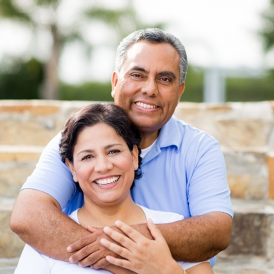 Smiling man and woman hugging after replacing missing teeth in Mesquite