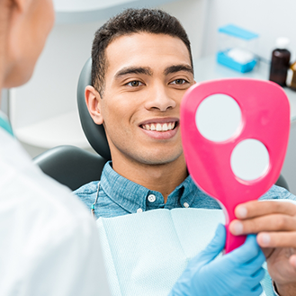 Man in the dental chair looking at his smile in a mirror
