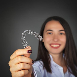 Smiling woman holding an Invisalign clear aligner