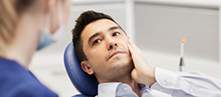 Man holding his cheek in pain while talking to his dentist