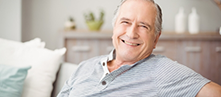 Man in a gray shirt smiling and sitting on a couch