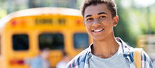 Teenage boy with braces smiling with a school bus in the background