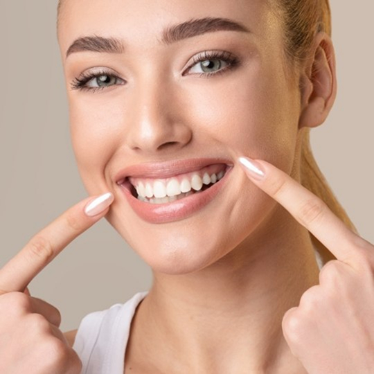Woman pointing to her smile after gum disease treatment in Mesquite