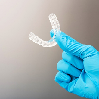 Hand in a latex glove holding a clear occlusal splint tray