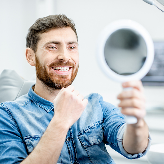 Dental patient looking in a mirror at his smile with veneers in Mesquite
