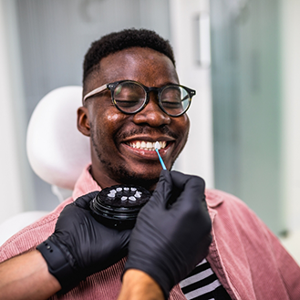Man grinning while a dentist holds a veneer in front of his teeth