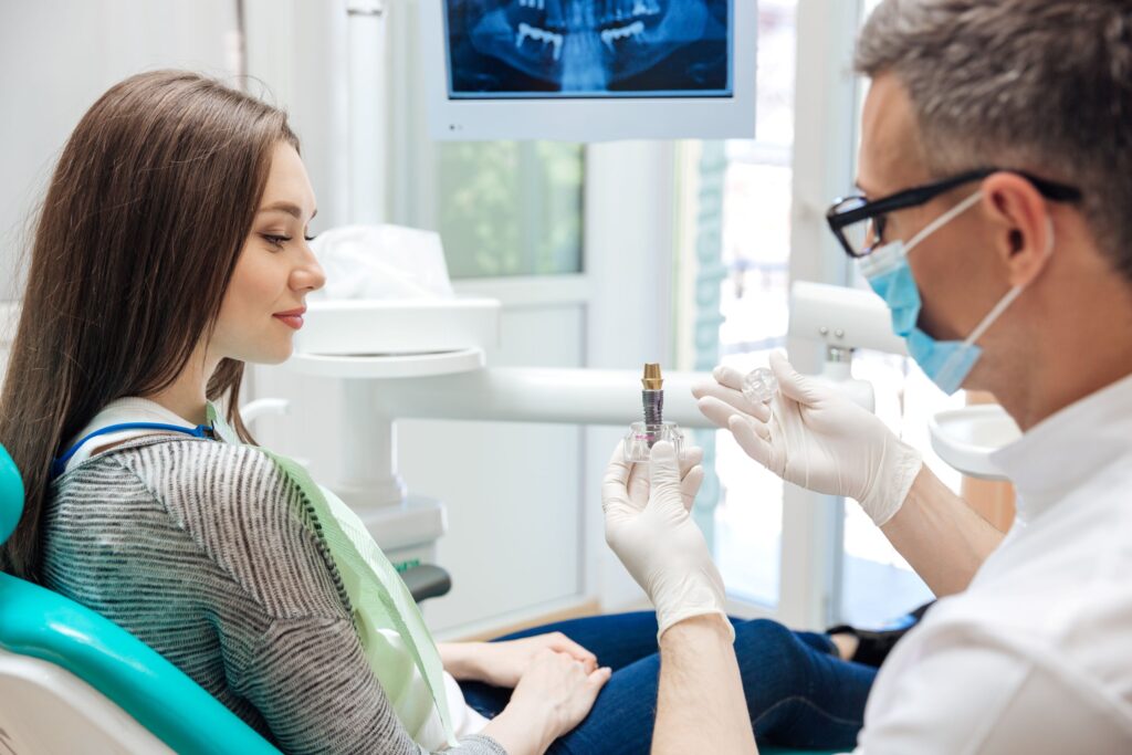 Dentist showing woman the parts of a sample dental implant