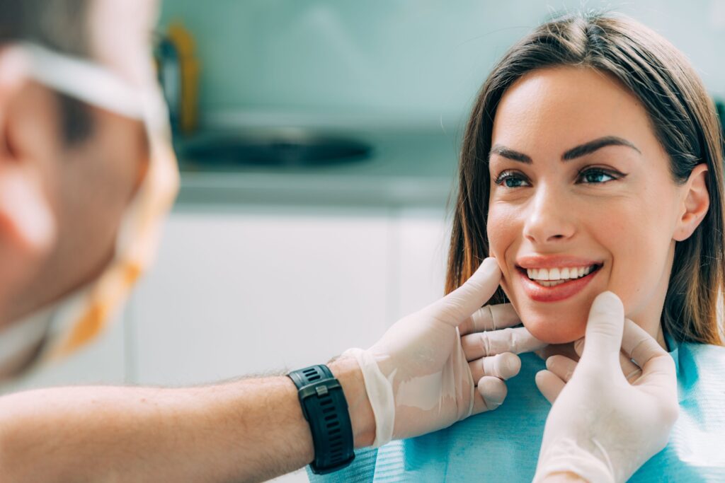 Woman smiling at dentist touching her cheeks with gloves on